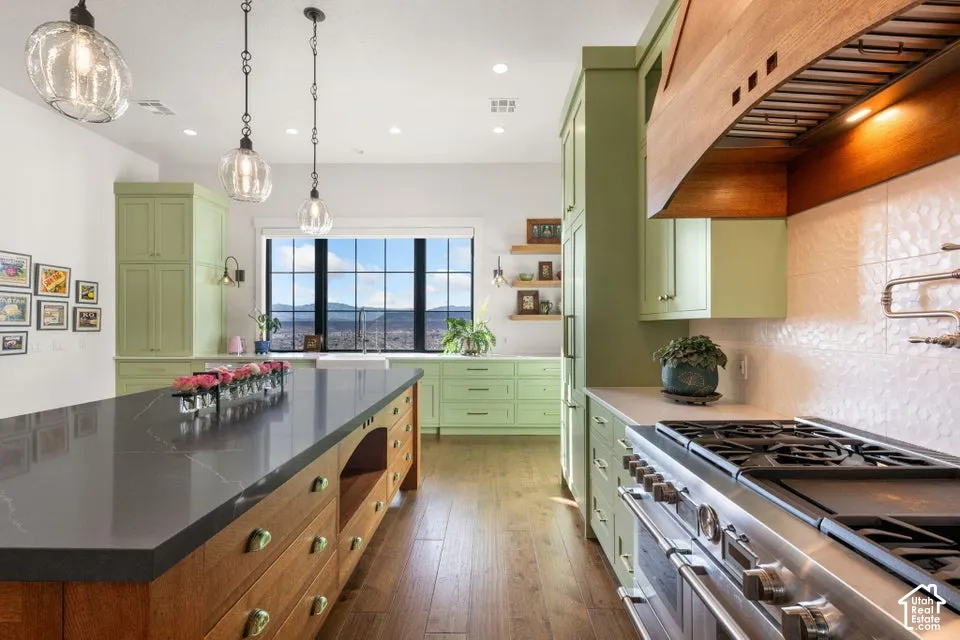 Expansive kitchen island with a dark stone countertop, light green cabinetry, stainless steel range, and wood-finish flooring
