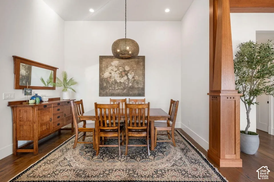 Formal dining room showcasing warm wood-finish flooring, a neutral patterned area rug, and rich wood cabinetry with integrated storage