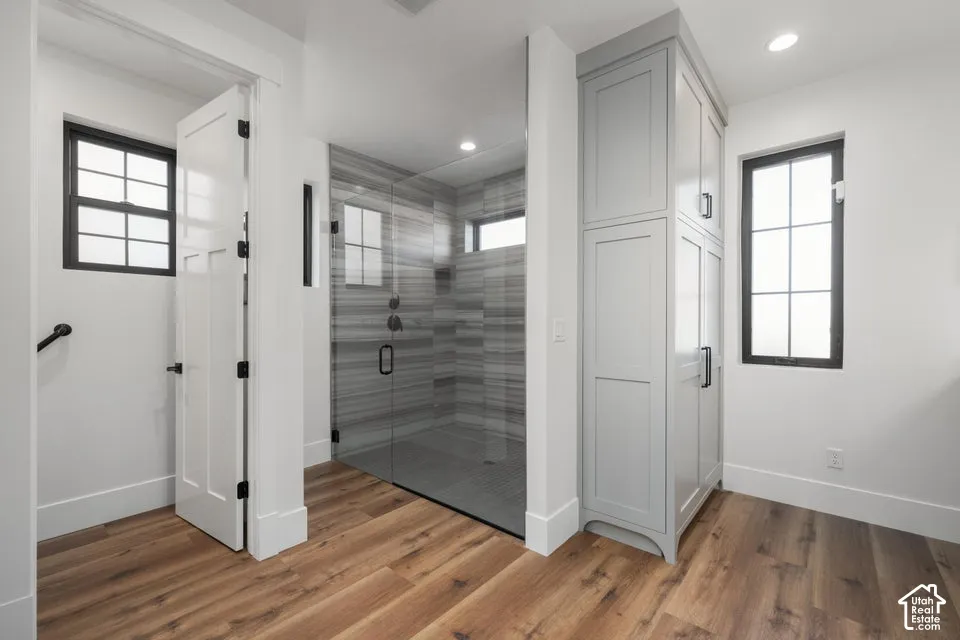Wood-finish flooring, full-height built-in storage cabinetry, large glass-enclosed shower with horizontally-stacked tile, and black-framed windows
