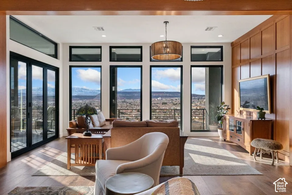 Expansive windows with transom panels, wood-finish flooring, a contemporary drum pendant light fixture, and wood-paneled wall