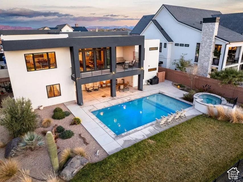 Modern residence featuring a resort-style backyard with illuminated saltwater pool, spa, and surrounding hardscape terrace