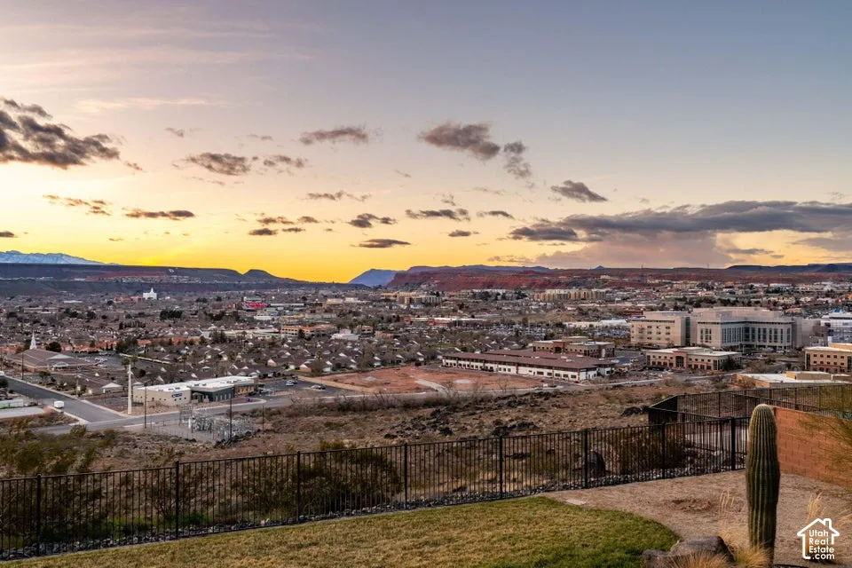 Expansive city and mountain landscape with a visible horizon and a metal fence
