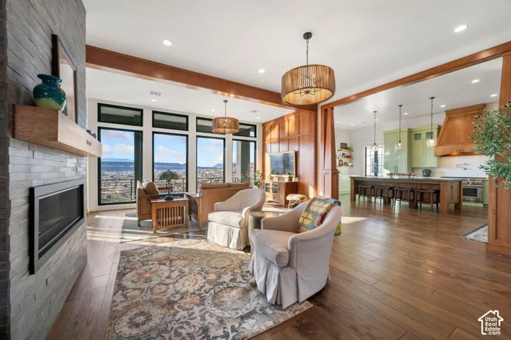 Hardwood flooring, floor-to-ceiling windows, stone-clad fireplace with mantel, exposed wood beams, and a large central kitchen island