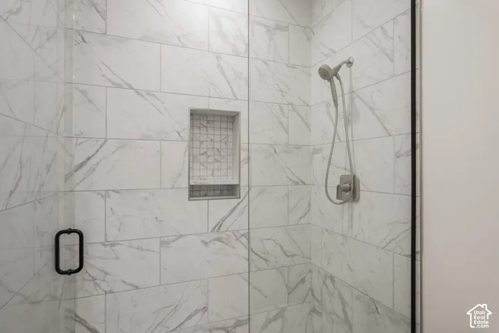 Walk-in shower featuring a glass enclosure, white tiled walls with grey veining, a built-in shower niche with mosaic tile, and a brushed nickel showerhead with handheld sprayer
