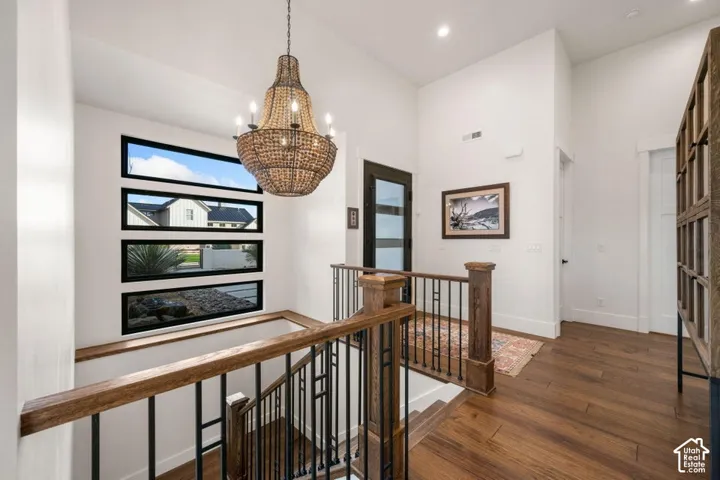 Vaulted ceiling with a beaded chandelier, wood-finish flooring, custom wood and wrought iron staircase, black-framed horizontal windows, and a black-framed glass-paneled door