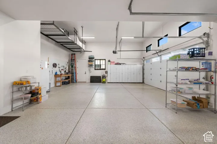 Spacious garage with epoxy flooring, white paneled garage doors, overhead storage racks, built-in cabinetry, and transom windows
