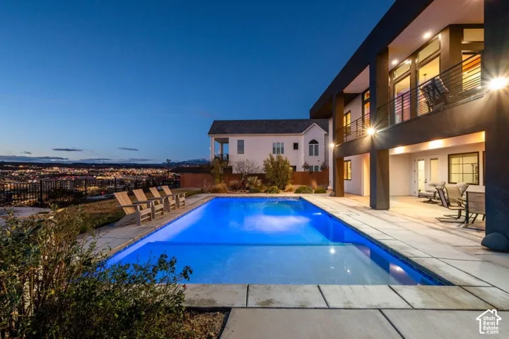 Rectangular inground pool with stone coping, concrete patio, and upper-level balcony with metal railing