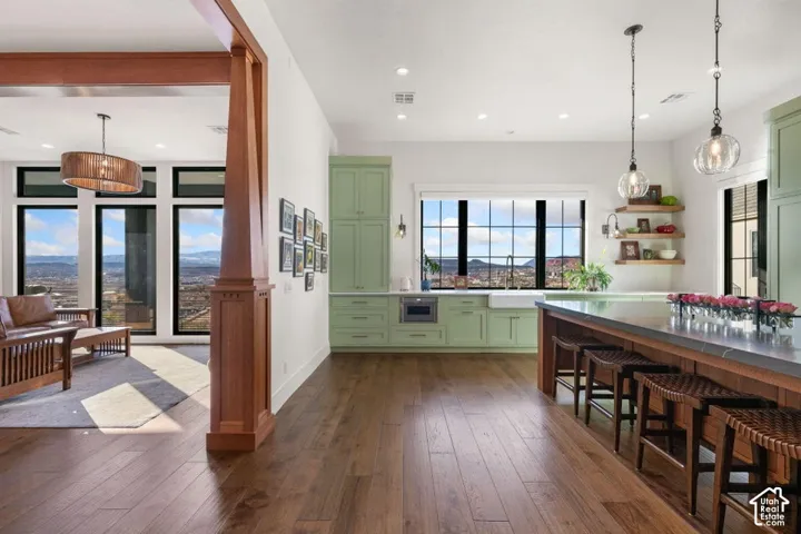 Hardwood flooring throughout, kitchen with sage green cabinetry, island with countertop seating, large windows, and a built-in farmhouse sink