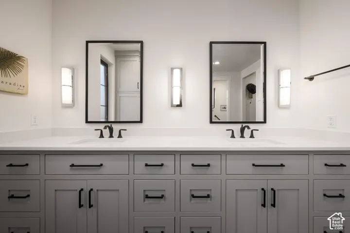 Dual rectangular mirrors with black frames, sconce lighting, an expansive vanity with double sinks, light-colored countertops, and shaker-style cabinetry with matte black hardware