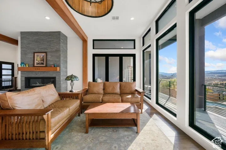 Spacious living area with a floor-to-ceiling stone fireplace, wood mantel, exposed wood beams, and a wall of large windows opening to a balcony