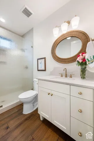 White vanity with brushed gold hardware, stone countertop, wood-finish flooring, and a glass-enclosed shower