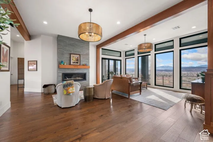 Spacious interior featuring wood-finish flooring, a contemporary fireplace with a stone surround and wood mantel, large windows with black frames, exposed wood beams, and recessed lighting