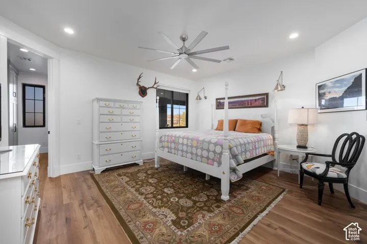 Spacious primary bedroom featuring hardwood flooring, a ceiling fan with integrated lighting, and abundant natural light from multiple windows