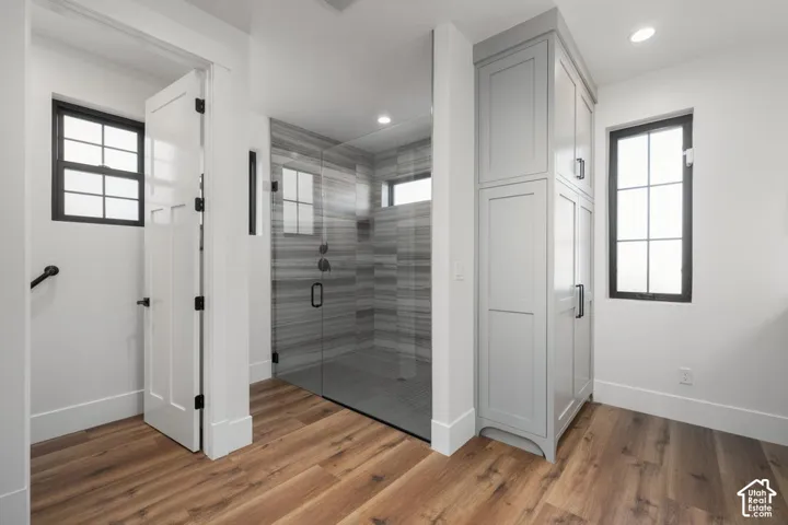 Wood-finish flooring, full-height built-in storage cabinetry, large glass-enclosed shower with horizontally-stacked tile, and black-framed windows
