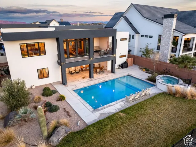 Modern residence featuring a resort-style backyard with illuminated saltwater pool, spa, and surrounding hardscape terrace