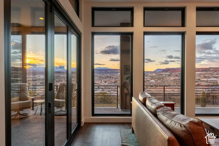 Expansive floor-to-ceiling windows with black framing, wood-finish flooring, and a sliding glass door opening to an exterior balcony with metal railings