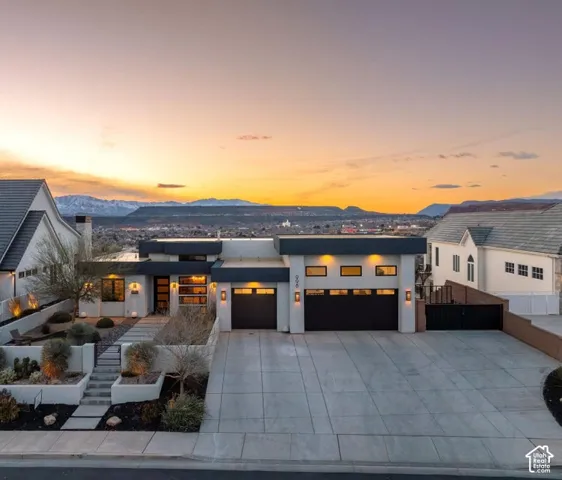 Modern exterior architecture with a flat roof, multi-level landscaping, an expansive concrete driveway, and integrated garage doors