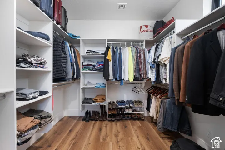 Expansive custom closet featuring wood-finish flooring, built-in shelving, multiple hanging rods, and recessed lighting