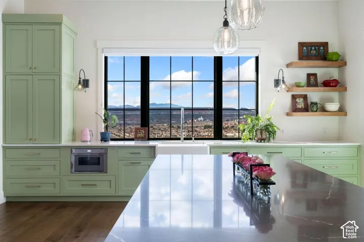 Kitchen featuring sage cabinetry, a large gridded window, wood-finish flooring, a built-in microwave, and pendant lighting