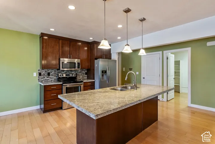 Kitchen featuring a large island with a stone countertop, a stainless steel double sink, and three pendant lights