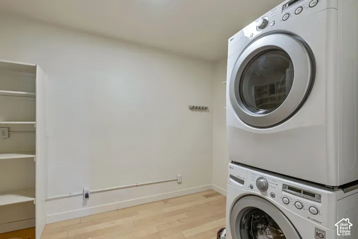 Laundry area featuring a stacked washer and dryer, built-in shelving, and wood-finish flooring
