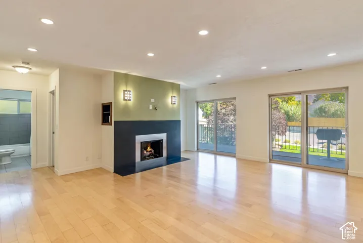 Hardwood-style flooring throughout, recessed ceiling lighting, built-in fireplace with a dark mantel, two sliding glass doors, and an adjacent bathroom with tiled walls