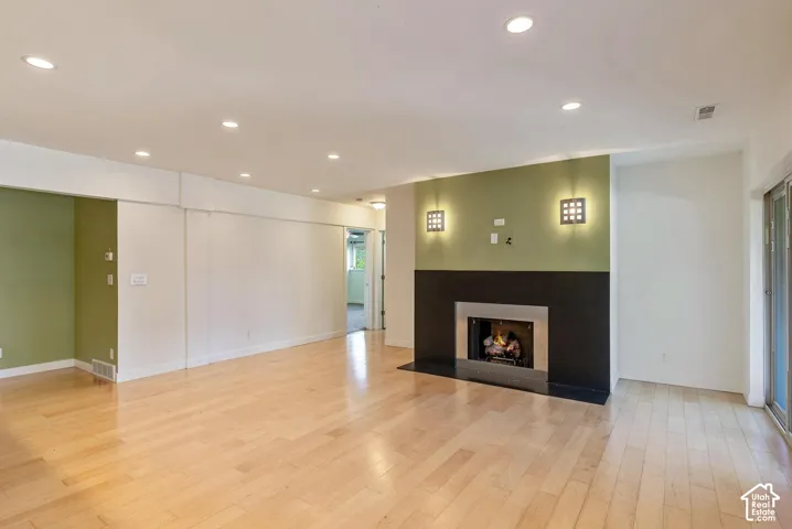 Wood-finish flooring, recessed lighting, built-in fireplace with a dark surround, and dual wall sconces