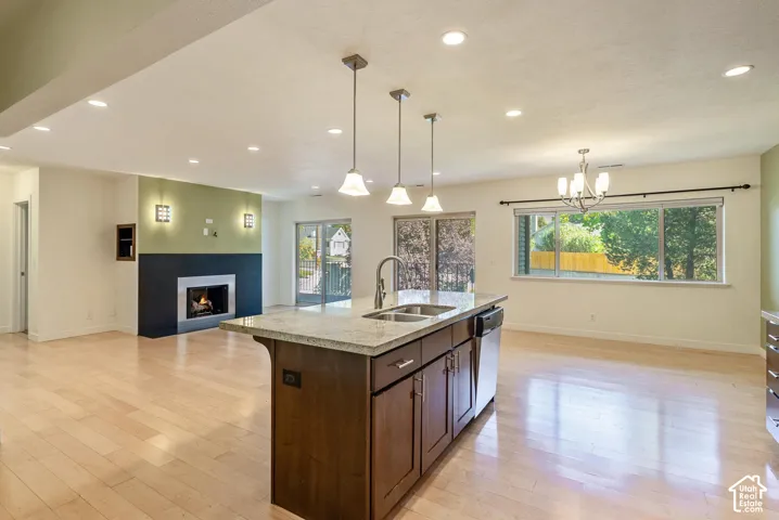 Spacious open-concept interior featuring light wood-finish flooring, a contemporary fireplace, and a kitchen island with a double sink and integrated dishwasher