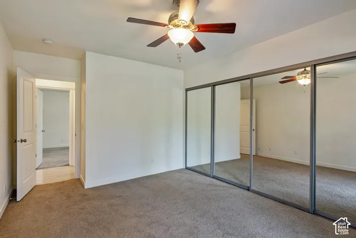 Wall-to-wall mirrored closet doors, ceiling fan with integrated lighting, neutral-toned carpeting, and a white paneled door