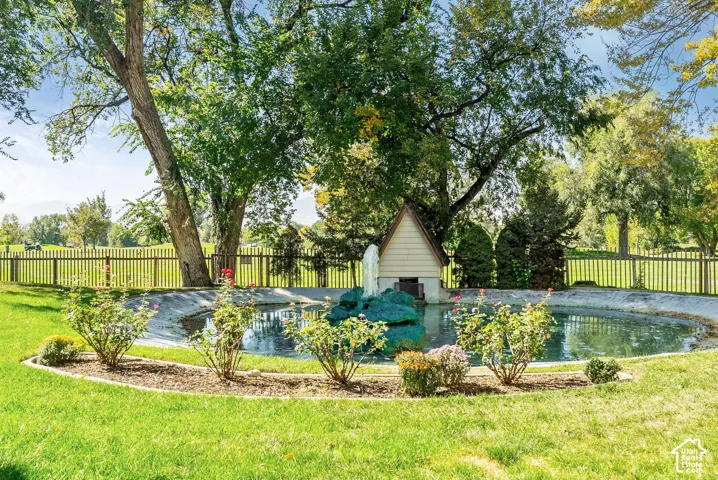 Expansive exterior featuring a pond with a fountain, mature trees, and a wooden fence