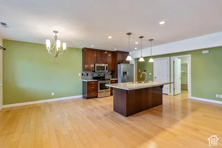 Hardwood-finish flooring throughout, kitchen island with built-in sink, pendant lighting, stainless steel appliances, and wood cabinetry