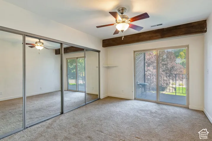 Sliding mirrored closet doors, ceiling fan with integrated lighting, wood-finish beam accent, sliding glass door, and private balcony
