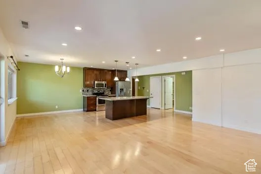Wood-finish flooring, recessed ceiling lighting, a kitchen island, pendant lighting, and stainless steel appliances