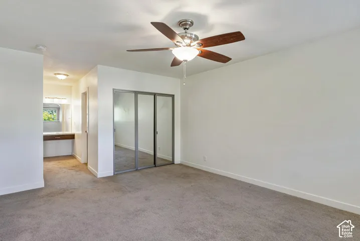 Ceiling fan with light fixture, carpet flooring, mirrored closet doors, and a built-in vanity with a window
