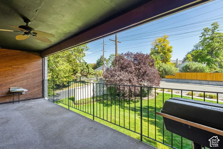 Expansive covered balcony featuring a ceiling fan, wood-finish accent wall, and wrought iron railings