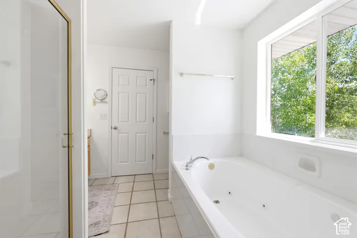 Soaking tub with integrated jets, framed window, tile flooring, glass-enclosed shower, and a paneled interior door