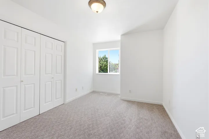 Bright secondary bedroom showcasing neutral carpet flooring, a large closet with white panel doors, and a sunny window with natural light