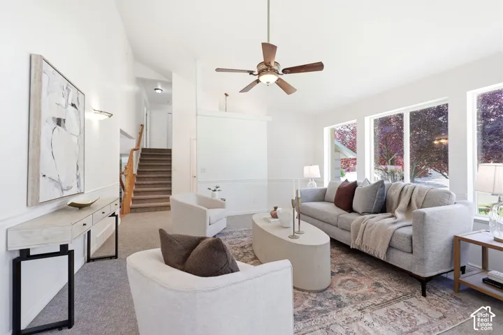 Vaulted ceiling with an installed ceiling fan, large windows, wood staircase, and wall sconce lighting