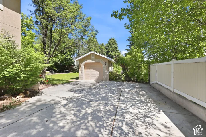 Detached garage with arched entry, concrete driveway, lush landscaping, and a privacy fence