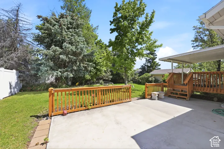 Expansive concrete patio with a wood-railed deck and covered carport