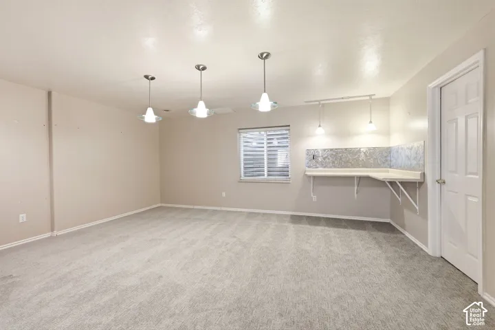 Spacious room featuring light-toned carpeting, a built-in corner desk with a patterned backsplash, and multiple ceiling-mounted pendant light fixtures