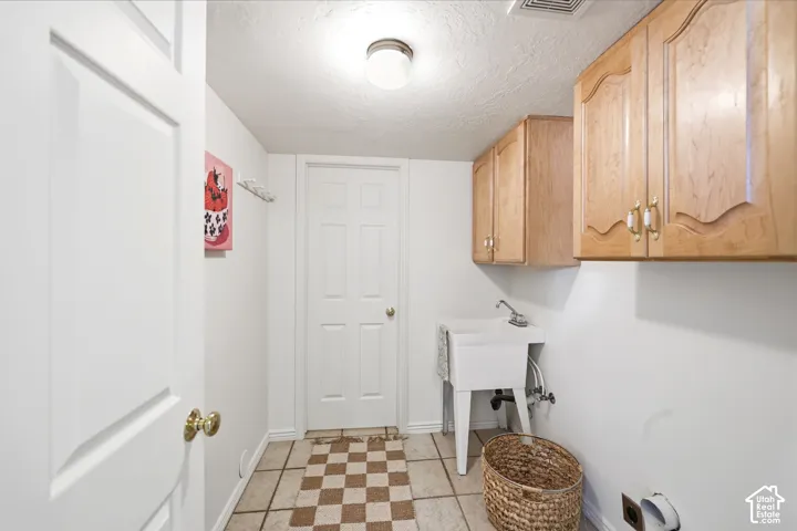 Laundry area featuring wood-finish cabinetry, a utility sink, and tiled flooring
