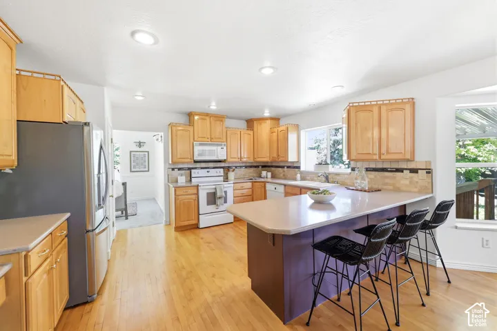 Kitchen featuring a peninsula island, light wood cabinetry, white appliances, and wood-finish flooring
