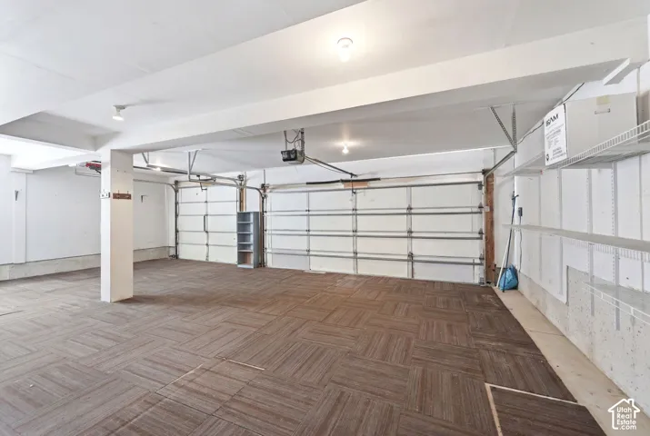 Spacious garage with multiple overhead doors, overhead lighting, patterned floor tiles, and integrated shelving units