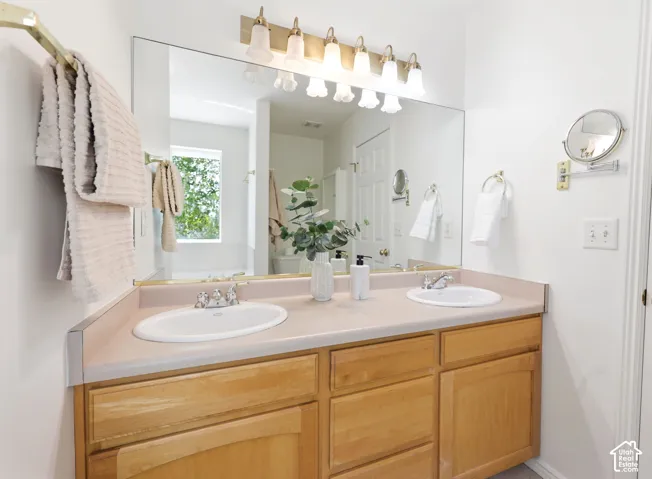 Double vanity with wood-finish cabinetry and integrated sinks, illuminated by a multi-bulb fixture