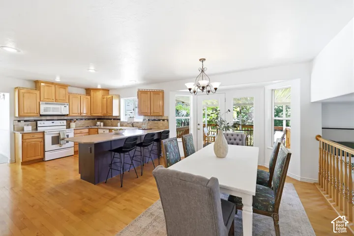 Hardwood flooring throughout, kitchen with wood cabinetry and tile backsplash, kitchen island with seating, double french doors, and a decorative chandelier