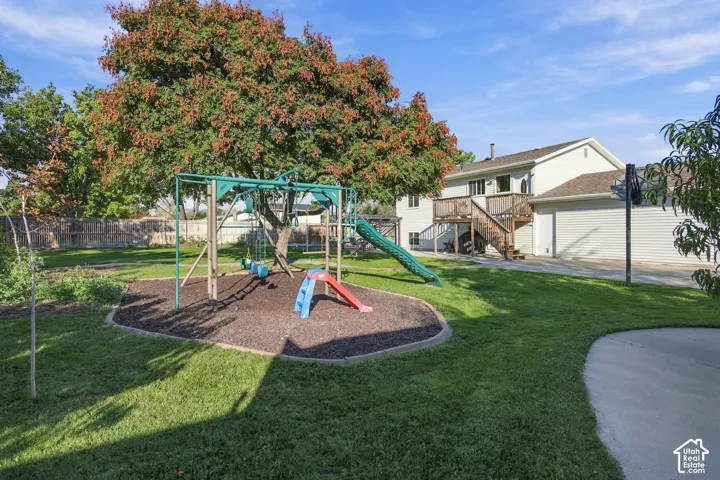 Spacious backyard with a vibrant green lawn, mature trees, a dedicated play area with wood chip ground cover, and a concrete patio