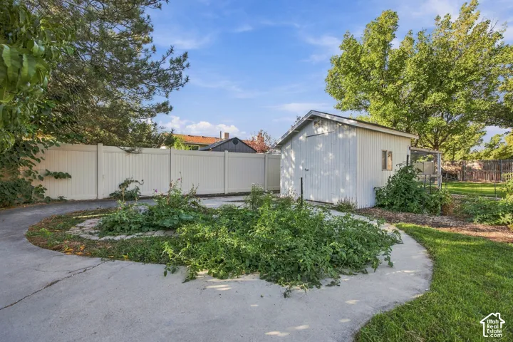 Detached storage shed with a window and white siding, concrete pathways, and a privacy fence