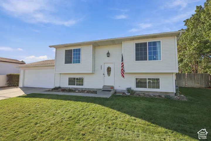 Split-level residence featuring white siding, an attached two-car garage, a concrete driveway, and a front lawn