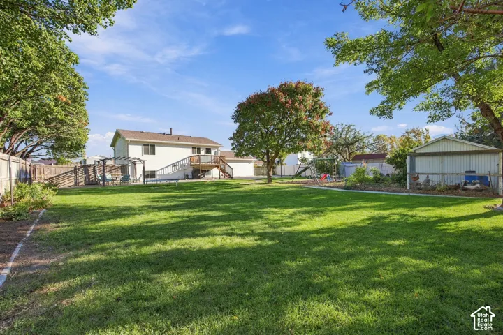 Expansive backyard featuring a manicured lawn, established trees, a two-story residence with a deck, and a detached storage shed